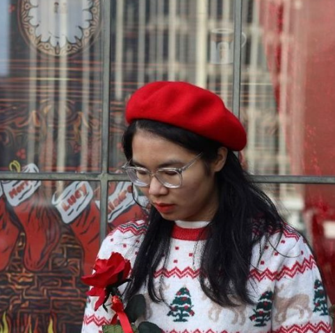 Huong a Vietnamese student in her early 20s wears a red beret and a christmas jumper and holds a rose